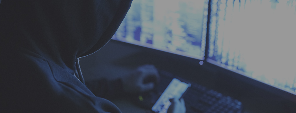 Man with a black hoodie using phone to hack into a computer screen